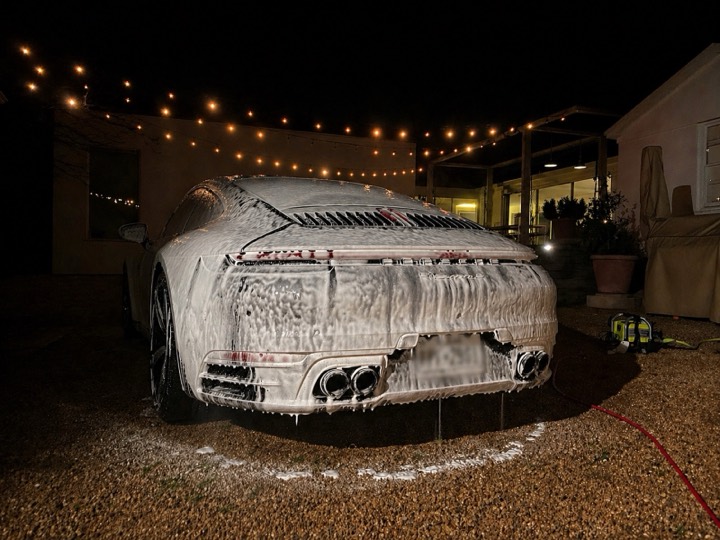Porsche 911 covered in thick foam during an evening wash under string lights, Westlake Hills Austin